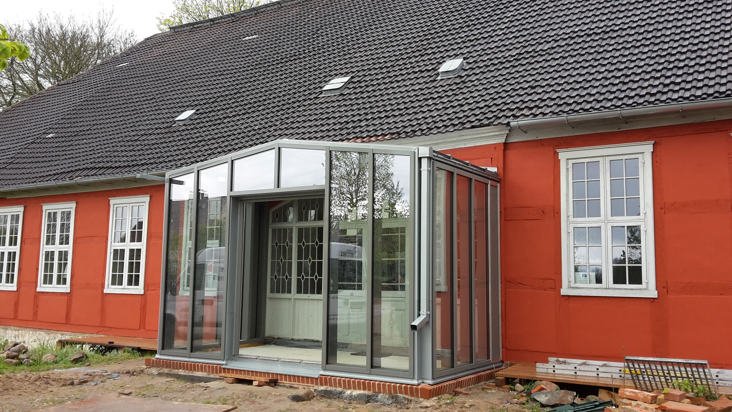 Gläserner Windfang vor rot gestrichenem Haus