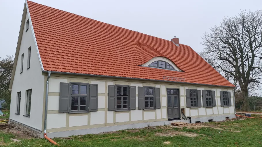 Saniertes Haus mit Grauen fenstern mit Fensterläden, dazu eine Fledermausgaube im Rotschindeldach